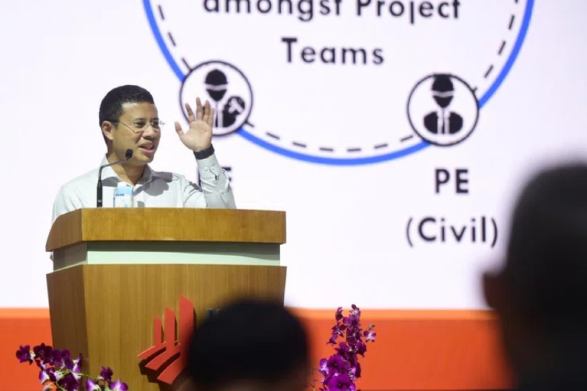 Speaker at podium gesturing during a construction industry presentation.